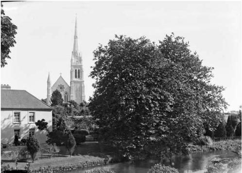 view of Holy Rosary Church with part of Midleton House, The Rock, and the Roxborough or Dungourney River in the foreground. This photo dates from after 1908, the year the church spire was completed. Note the extensive and elaborate gardens. (National Library of Ireland.)